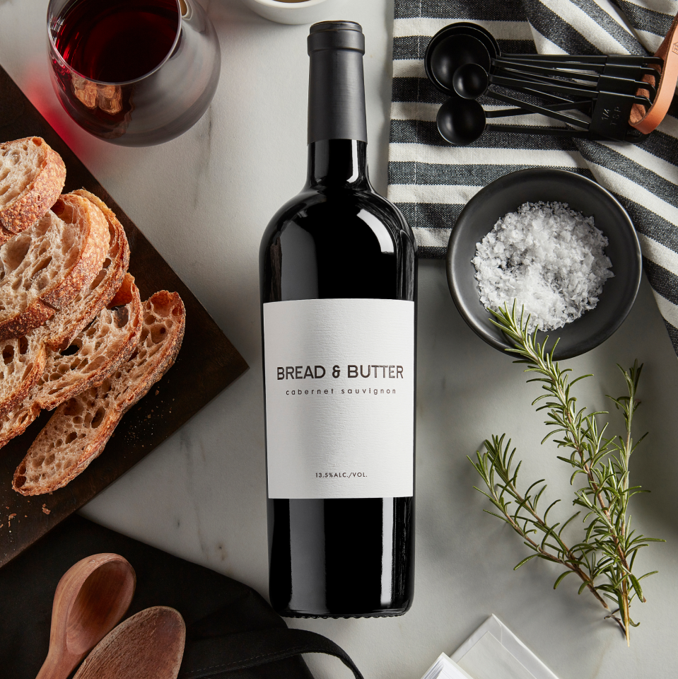 Bread & Butter Cabernet Sauvignon on a table with rosemary, salt, measuring spoons, bread and wine in a glass.