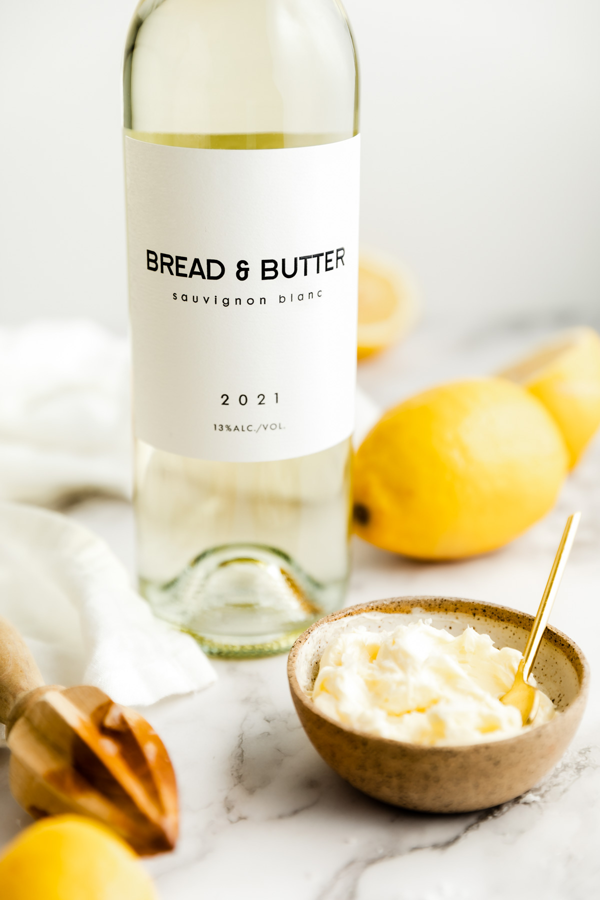 Bread & Butter Sauvignon Blanc on a marble table next to a bowl of lemon butter and lemons.