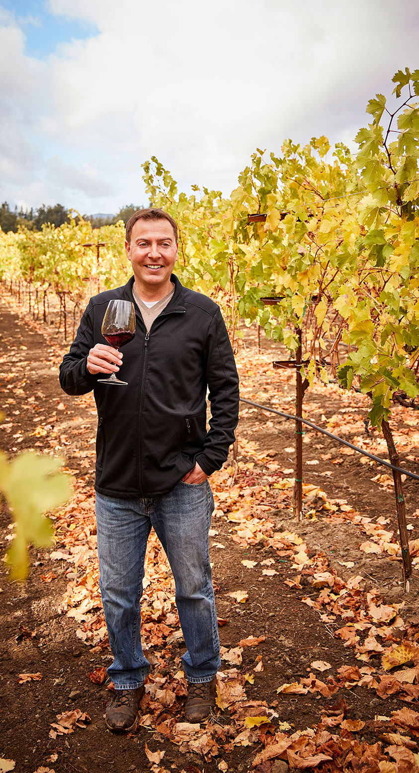 Bread & Butter Winemaker Matt Shuplock standing in the vineyards during autumn with a glass of red wine